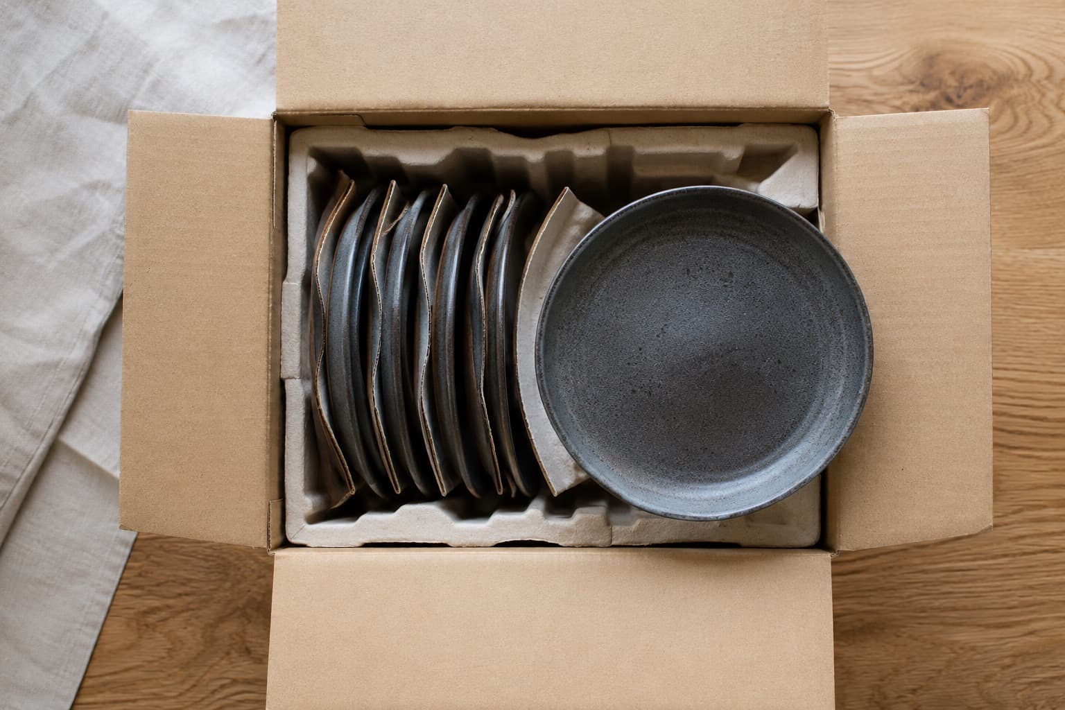 An open corrugated carton seen from above, fitted with moulded pulp trays holding plates upright on edge with fluted card separators between them.