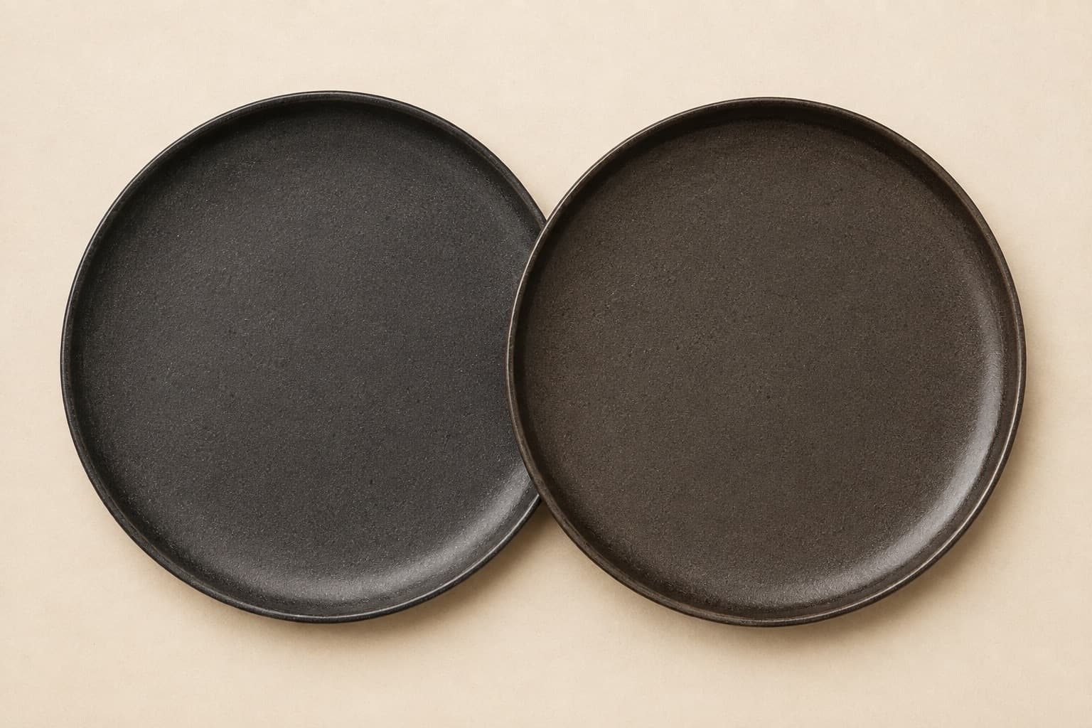 Two charcoal plates overlapping, one a cooler graphite and the other a warmer brown-black, showing the batch difference at the join.