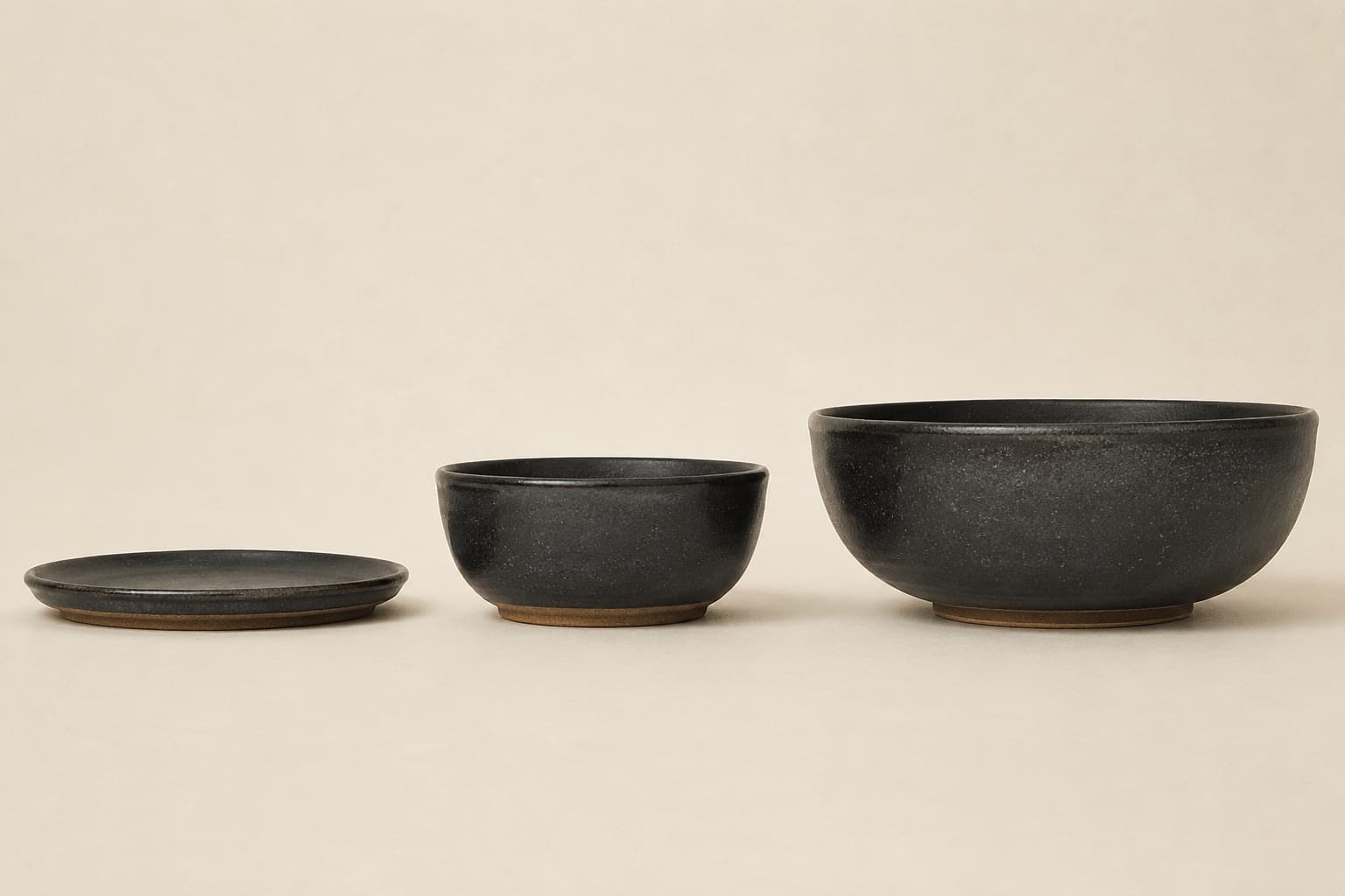 Three stoneware pieces in a row photographed square on: a flat plate, a deep bowl and a large mixing bowl, showing the depth difference that decides the category.