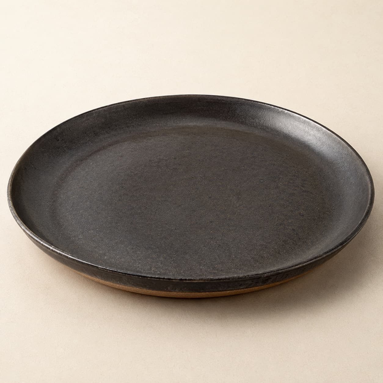 Chef Plate Ø30 — charcoal glazed stoneware with an unglazed clay foot ring.