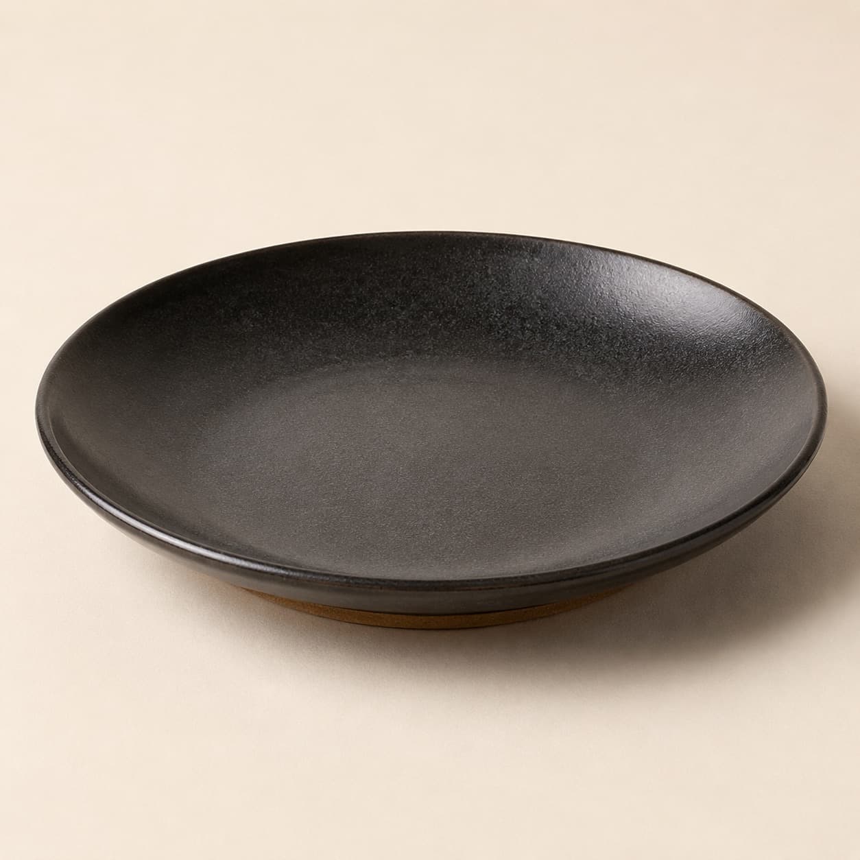 Coupe Plate Ø22 — charcoal glazed stoneware with an unglazed clay foot ring.