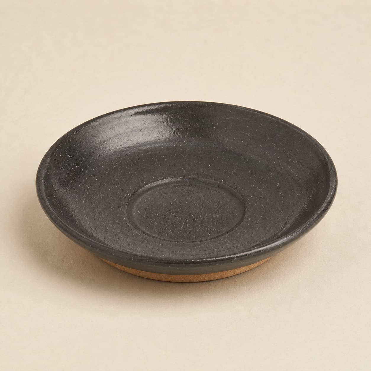 Saucer Ø16 — charcoal glazed stoneware with an unglazed clay foot ring.